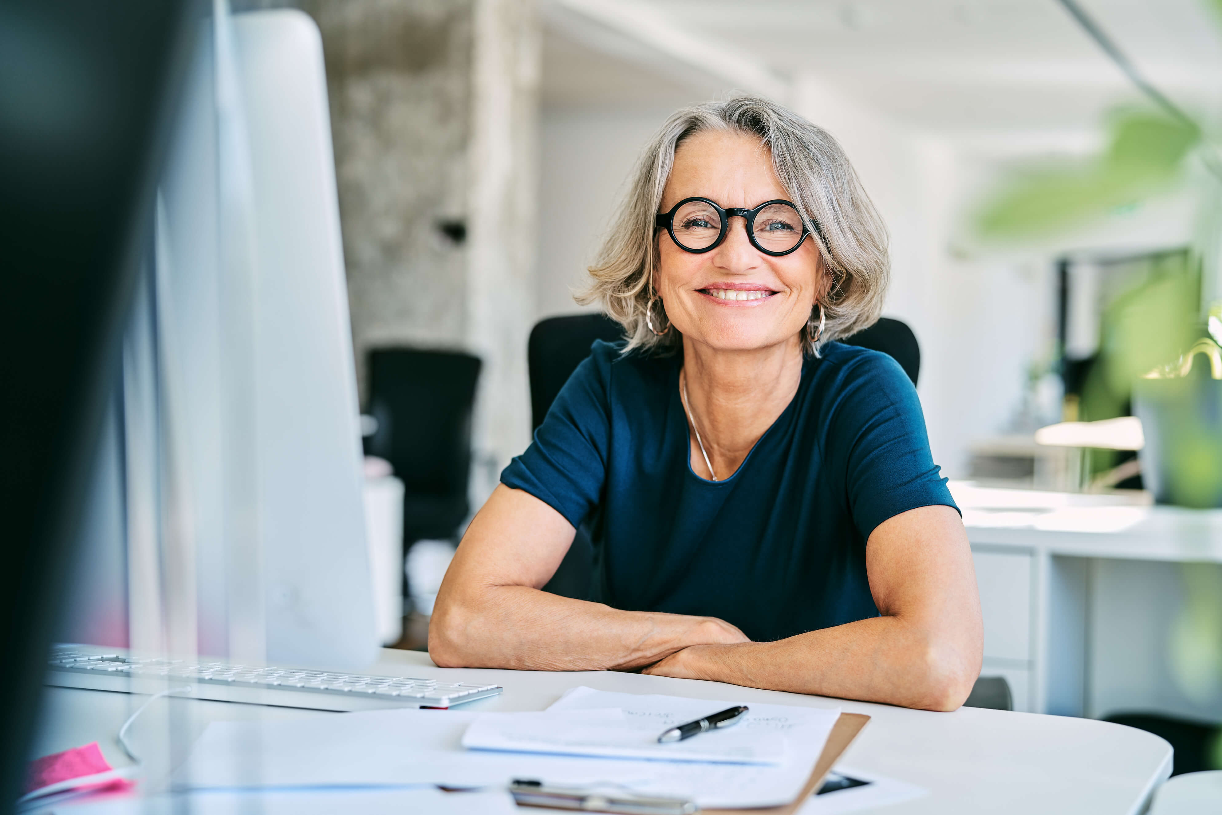 Lady with glasses sat at a work desk smiling